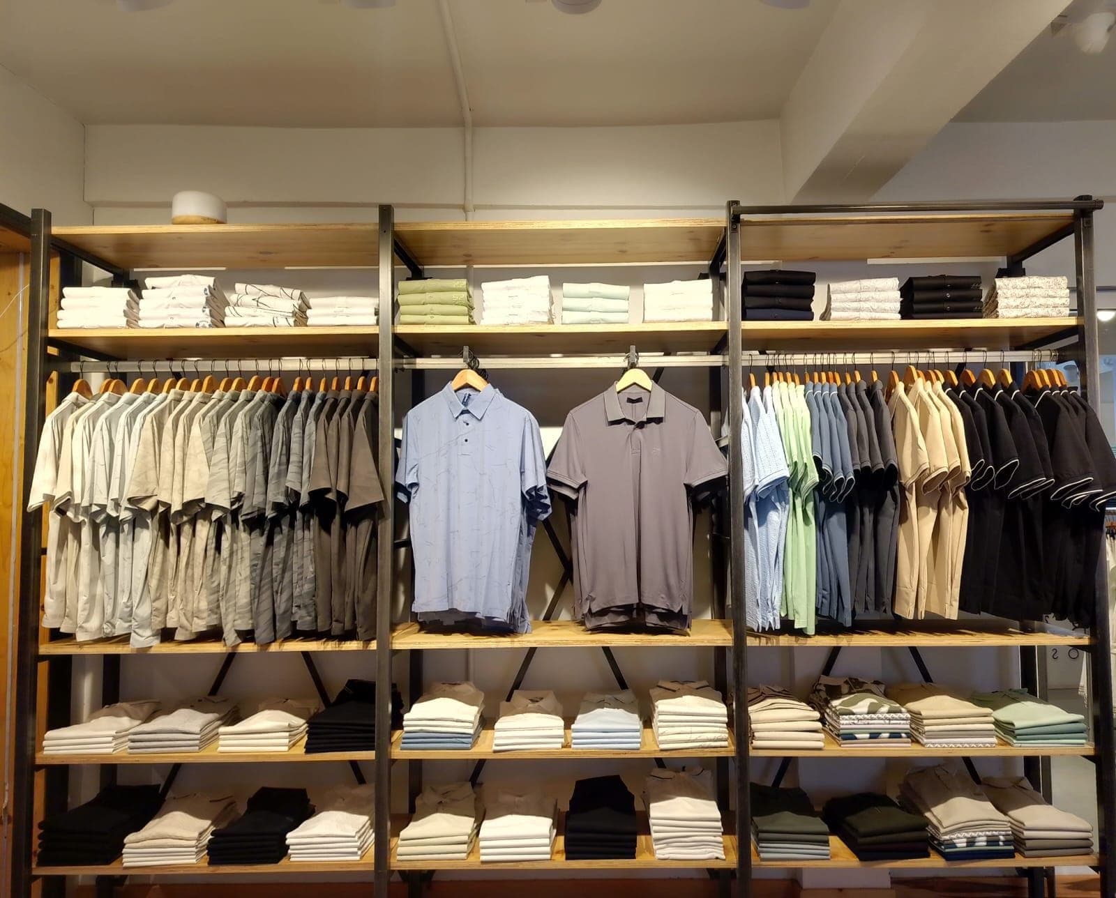 A wall of polos and folded shirts on timber and steel shelving, two polos hung at its centre