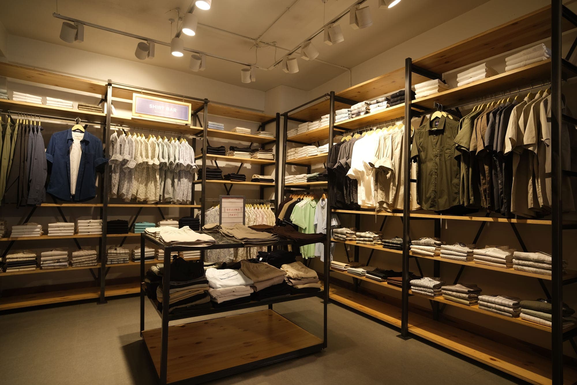 A store floor of shirt bays and hanging rails under track lights, stocked with the season's menswear